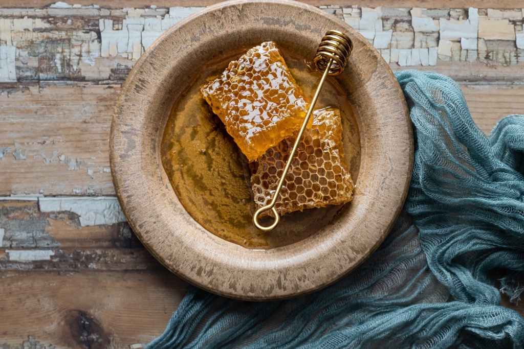 Honigwaben und Honig in brauner Schale auf einem Holztisch neben bläulichem Tuch