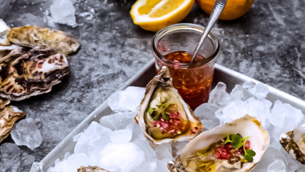 Obstessig in der maritimen Küche: Austern auf Eis mit Marinadeglas und aufgeschnittener Orange