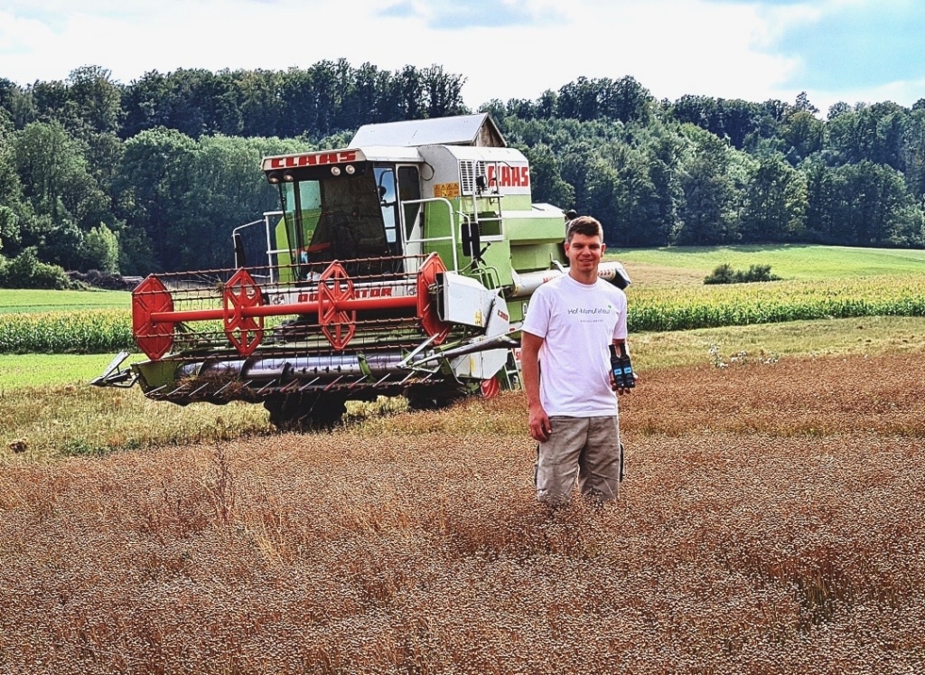 Tobias Kreiselmeier von der Hofmanufaktur Kreiselmeier steht auf dem Feld vor einem Traktor