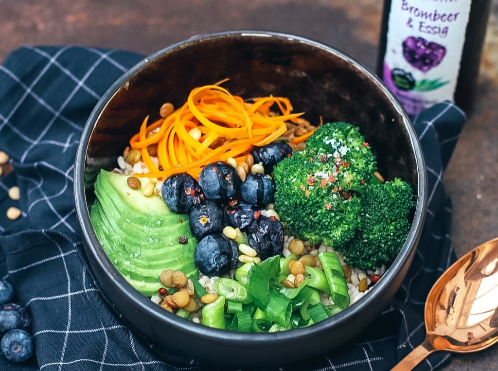 Essigsorten: Bowl mit Gemüse, Blaubeeren und Dressing neben Essigflasche