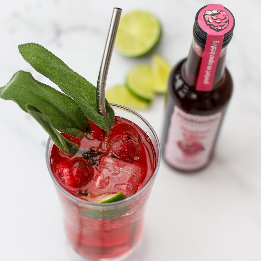 Drink mit rotem Fruchtessig neben Essigflasche - Essigsorten Himbeeressig lassen sich gut als Schorle trinken