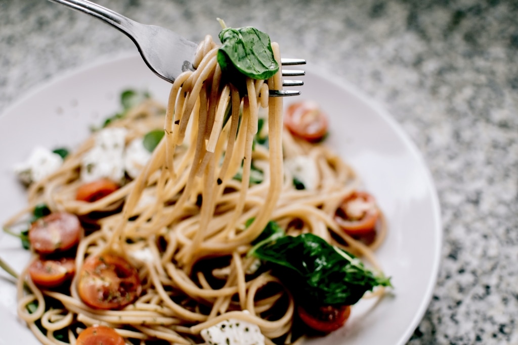 Spaghetti Caprese auf einem weißem Teller vor grauem Hintergrund
