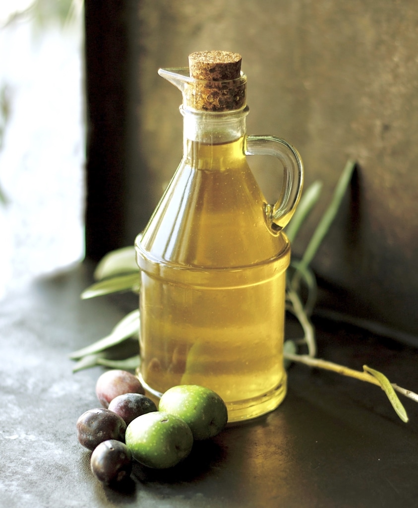 Verfeinert den Tomate Mozzarella Salat: Olivenöl in einer Glasflasche neben grünen und schwarzen Olivenfrüchten